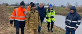p.o. Komendanta Powiatowego PSP w Wolsztynie kpt. Damian Glapiak patroluje stan wałów. Obok wót i pracownicy Wód Polskich.