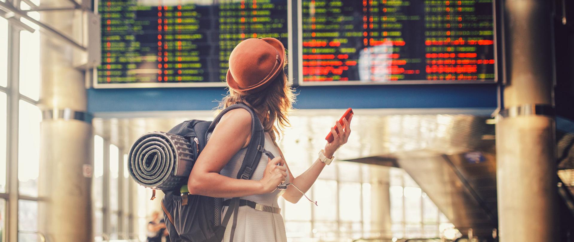 Dziewczyna z plecakiem, na lotnisku, z telefonem w ręce.