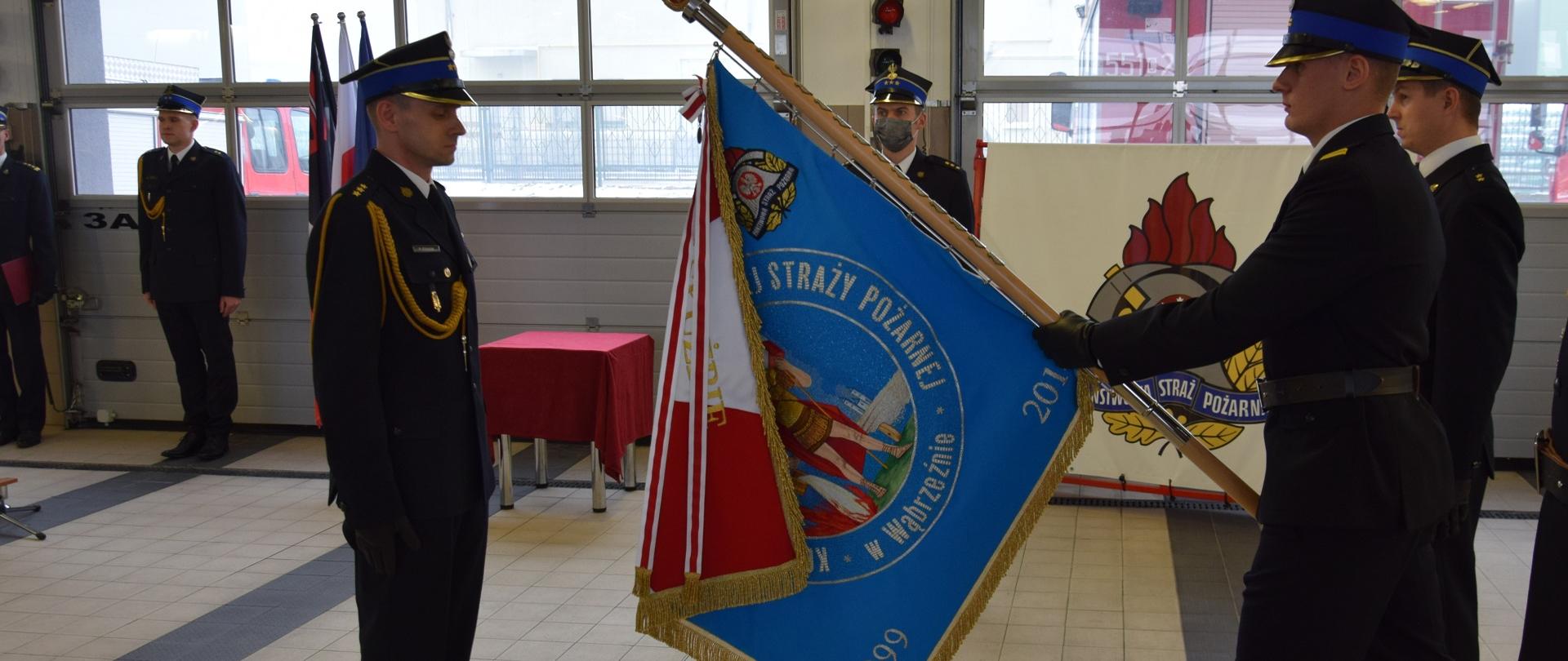 Na pierwszym planie stoi kpt. Robert Stasiak oraz poczet sztandarowy KP PSP w Wąbrzeźnie. W tle kpt. Dawid Krajnik oraz mł.kpt. Karol Dzielski.