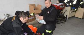Sprzęt pożarniczy dla ukraińskich strażaków. Komenda Powiatowa PSP w Rawiczu. Strażacy przygotowują do transportu sprzęt. Dwóch z nich pakuje do torby medycznej materiały opatrunkowe. W tle kartony z ubraniami, motopompa i węże.