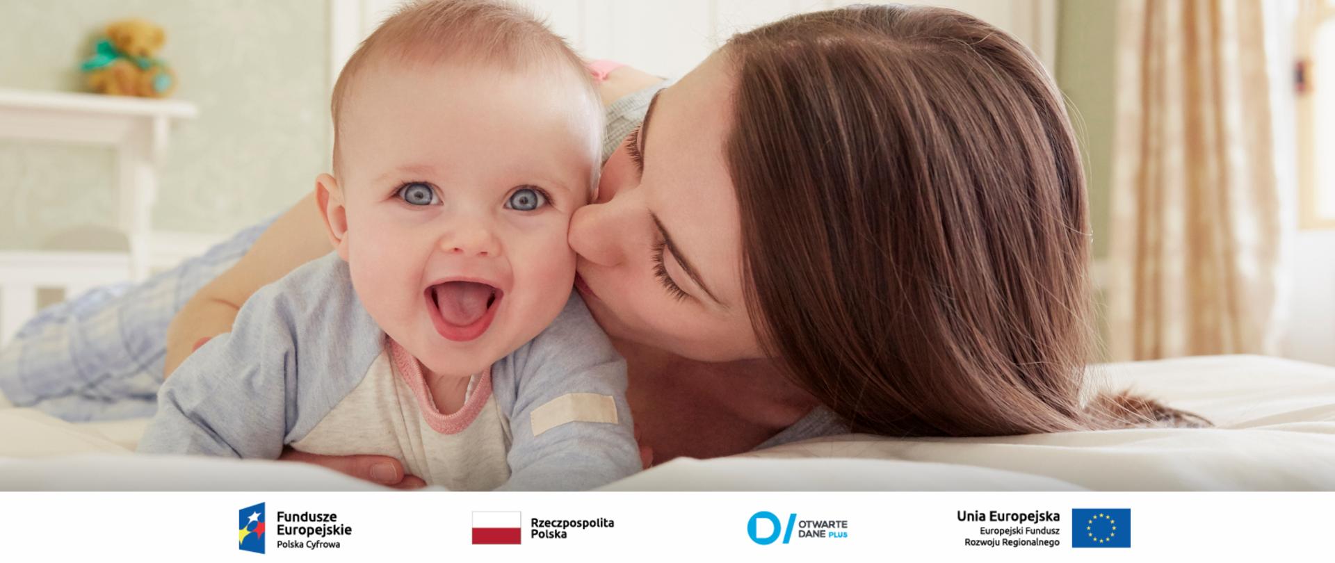 Na zdjęciu młoda kobieta całująca z policzek uśmiechnięte niemowlę.