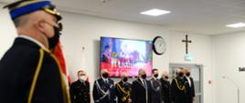 Strażacy Państwowej Straży Pożarnej stoją wraz z wojewodą pomorskim przed mikrofonami.