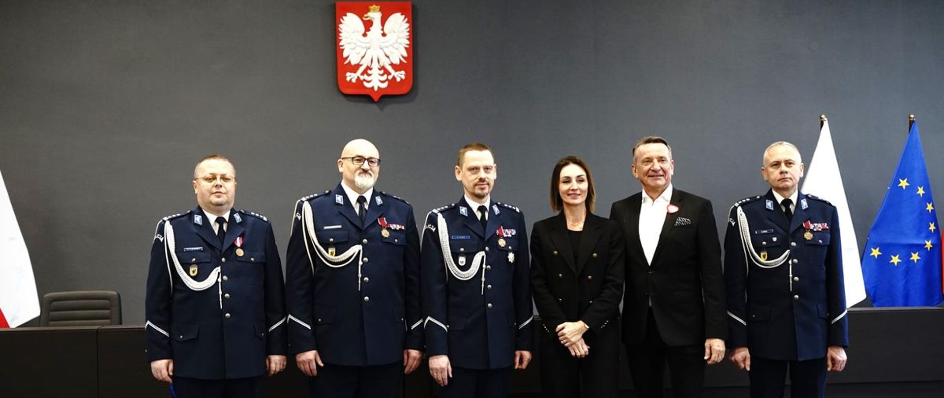 Na zdjęciu widać kobietę oraz pięciu mężczyzn. Czterech mężczyzn w galowych mundurach policji. 