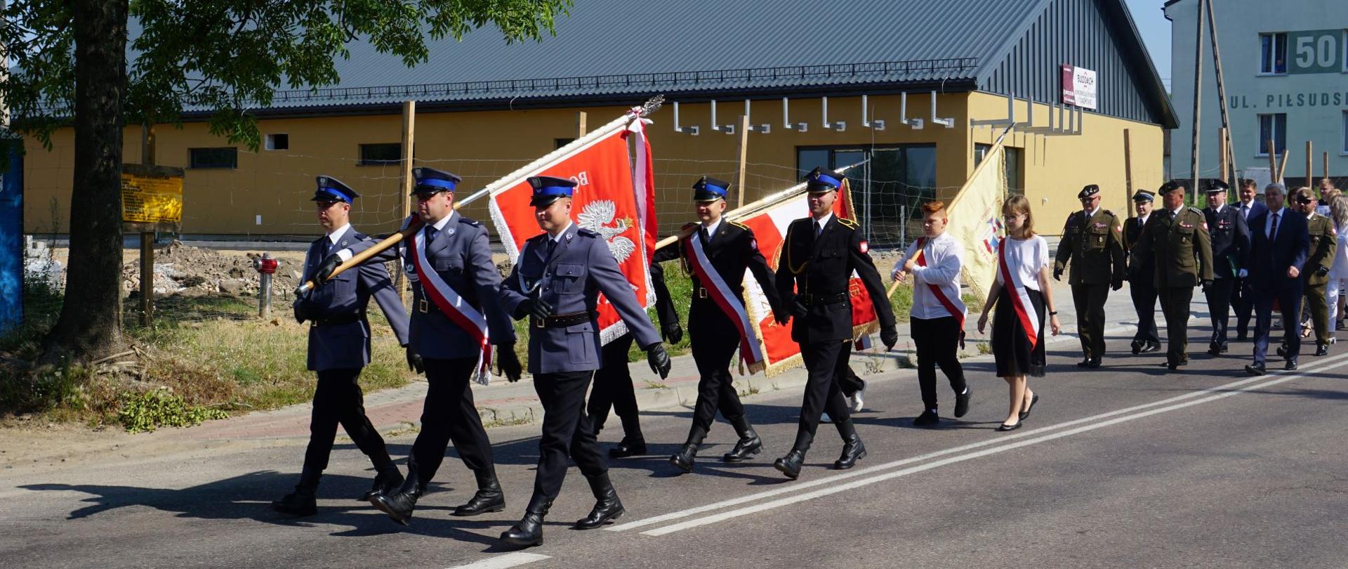 Po drodze maszerują trzy poczty sztandarowe. Za nimi idą wojskowi i inne służby mundurowe.