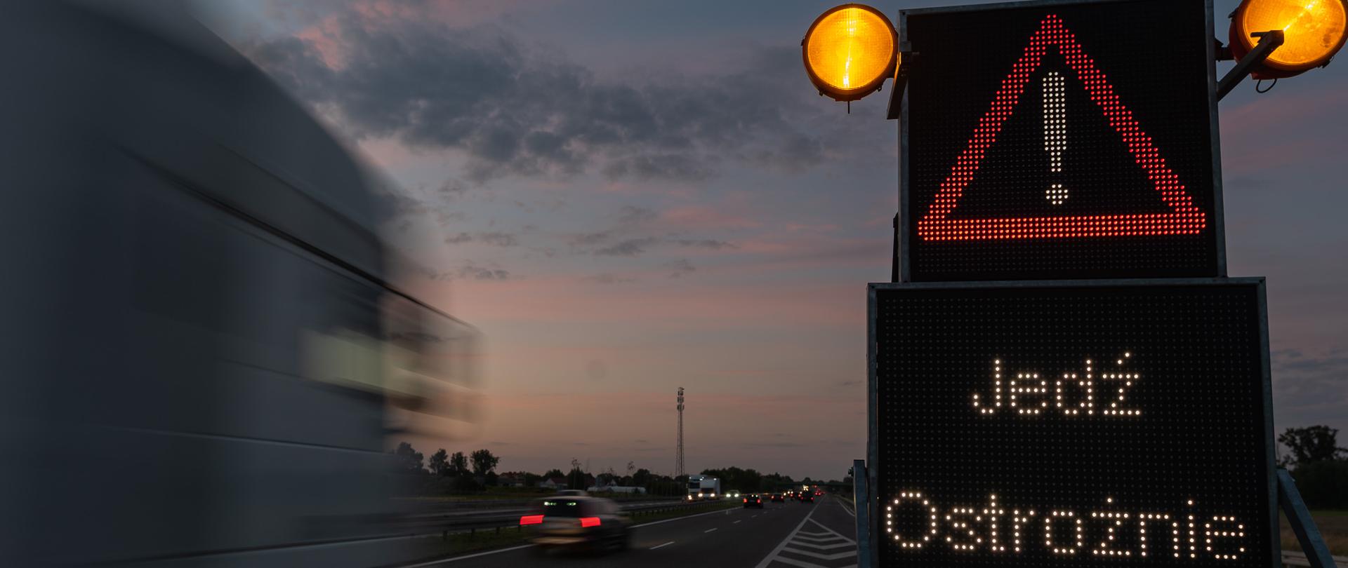 Na zdjęciu ruch pojazdów a na pierwszym planie znak "Jedź ostrożnie"