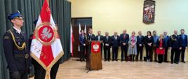 poczet sztandarowy KP PSP Kozienice na sali podczas Uroczystego wręczenia promes dla Młodzieżowych Drużyn Pożarniczych z terenu powiatów kozienickiego i białobrzeskiego obywającej się na sali gimnastycznej w tle stoją zaproszeni goście