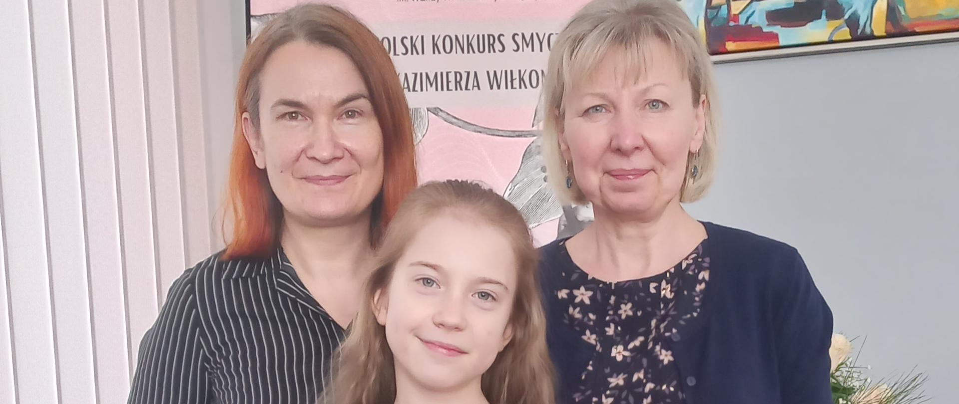 Uczennica ze skrzypcami i w obecności nauczycielek, w tle obraz