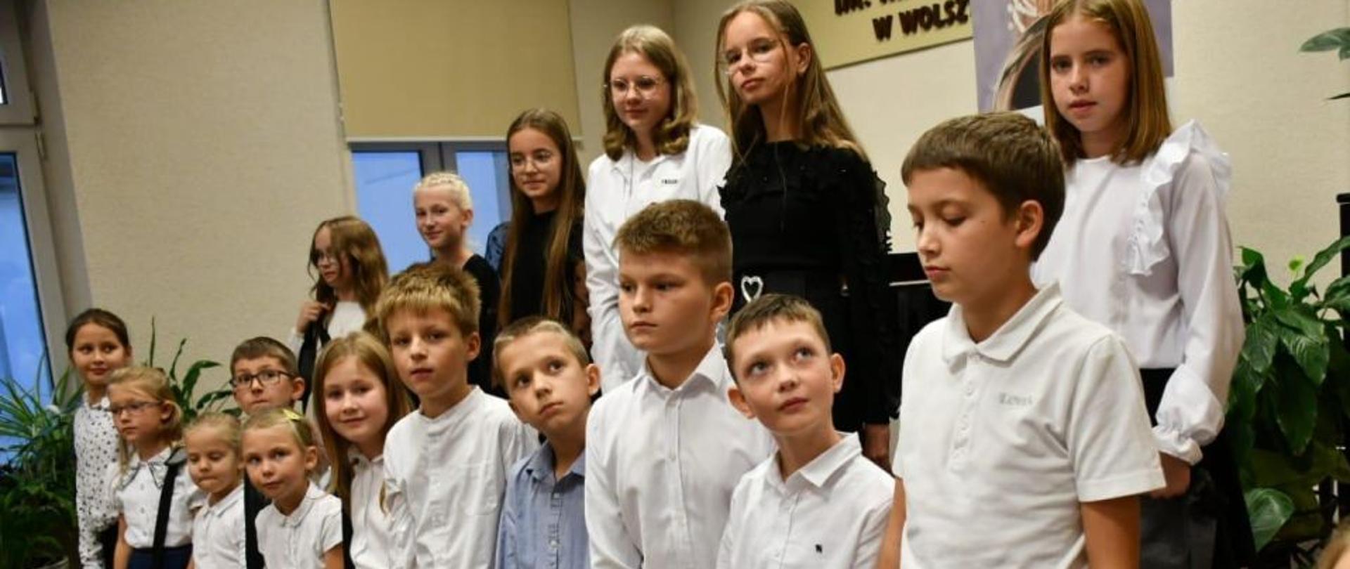 Uczniowie klas pierwszych stoją w dwóch rzędach. Każdy z nich trzyma podarunek- torbę.