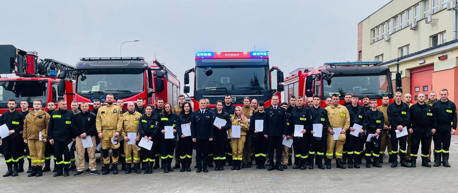 zdjęcie grupowe na tle samochodów pożarniczych uczestników szkolenia oraz funkcjonariuszy komendy