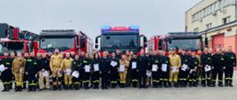 zdjęcie grupowe na tle samochodów pożarniczych uczestników szkolenia oraz funkcjonariuszy komendy