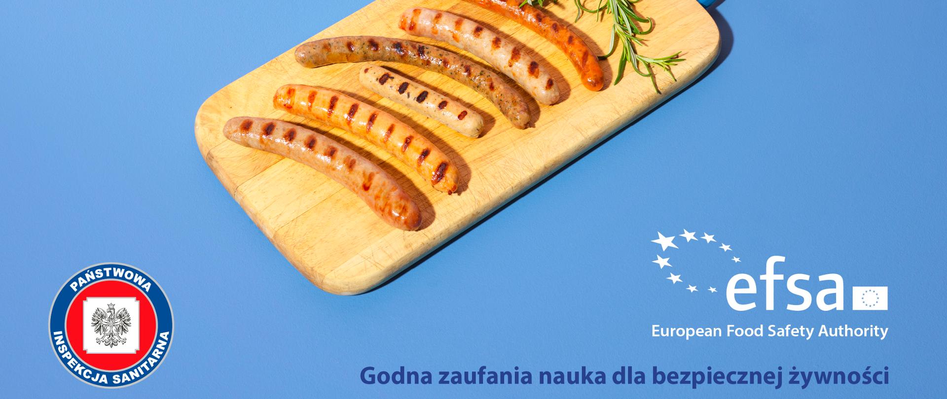 Zdjęcie przedstawia deskę, a na niej grillowane kiełbaski i gałązka rozmarynu. 