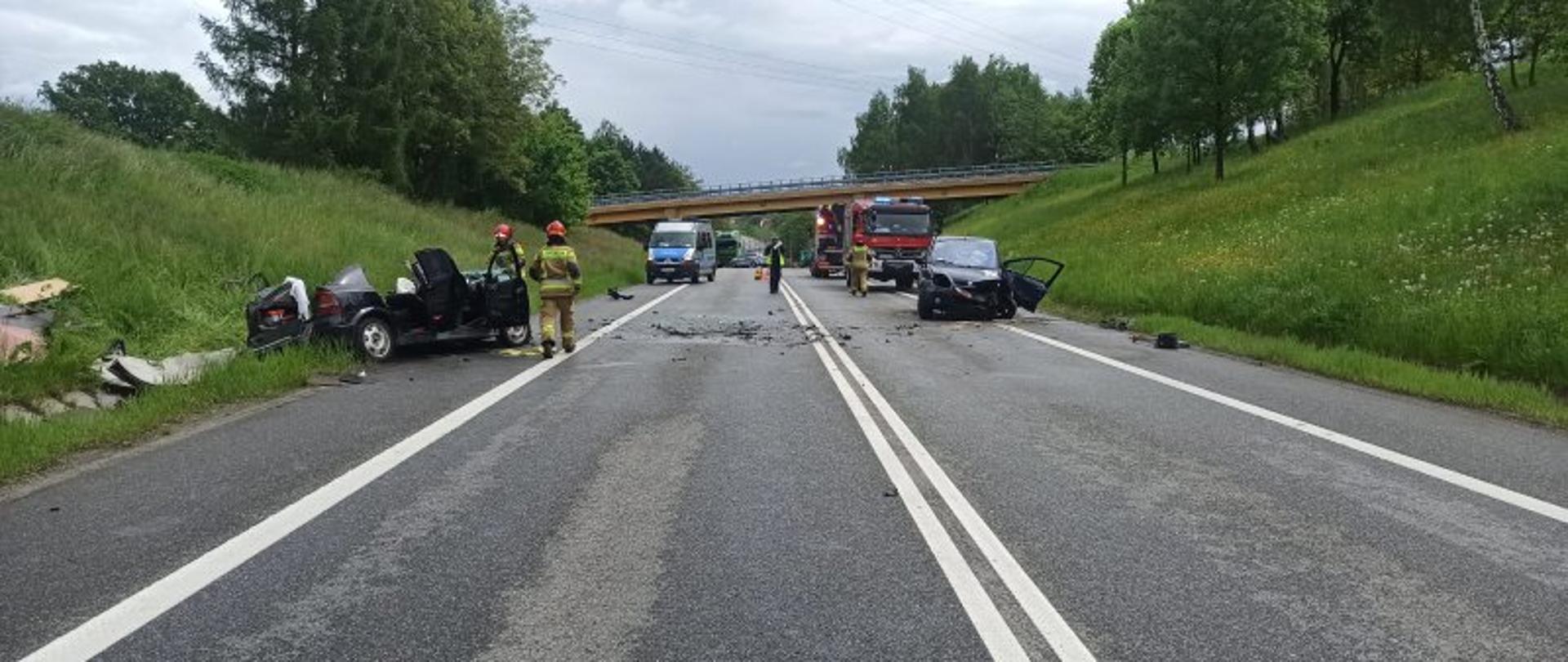 Zdjęcie przedstawia wypadek dwóch samochodów osobowych na DK94 obok Bochni. Jest pora dzienna. Jeden z samochodów biorących udział w wypadku znajduje częściowo poza pasem drogi krajowej. Samochód posiada odcięty dach w wyniku prowadzenia akcji ratowniczej. Drugi samochód znajduje się na prawym pasie ruchu posiada on uszkodzony przód oraz wyłamane drzwi od strony kierowcy. Na jezdni widać fragmenty uszkodzonych pojazdów. Na drugim planie widać radiowóz Policji z Bochni, jednego policjanta prowadzącego czynności dochodzeniowe na miejscu wypadku, dwa samochody Straży Pożarnej z Bochni oraz strażaka udającego się w kierunku pojazdu pożarniczego. 