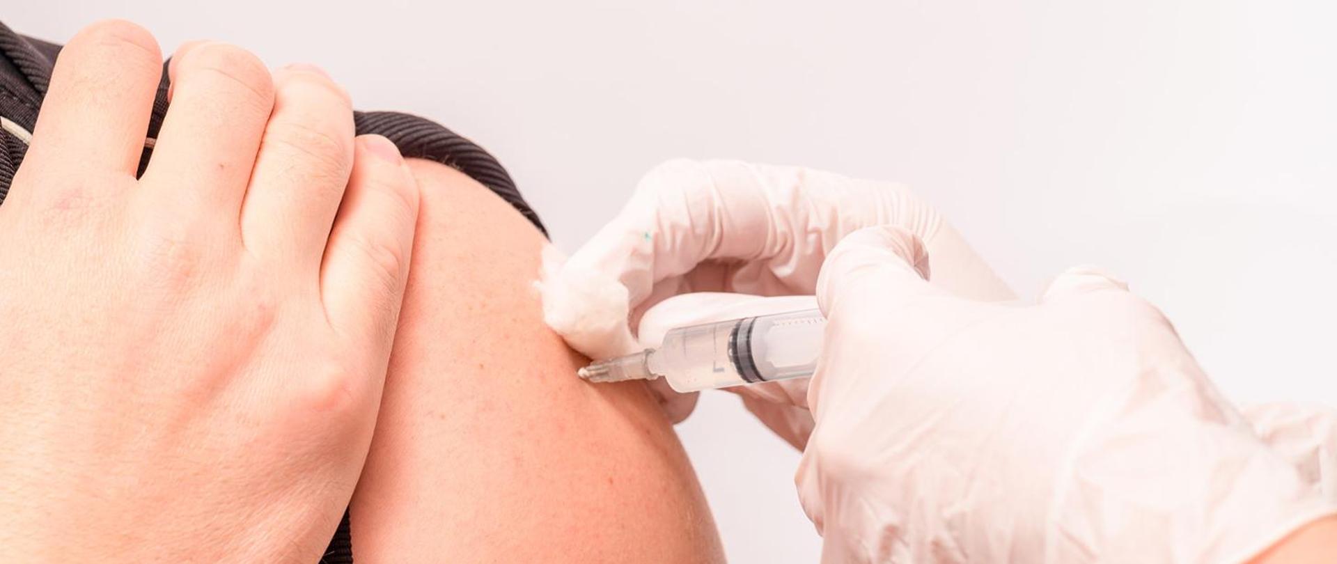 Obrazek przedstawia moment szczepienia w ramię.