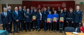 młodzieżowe drezyny pożarnicze MDP w towarzystwie parlamentarzystów władz wojewódzkich, powiatowych trzymają w ręku okolicznościowe promesy, wszyscy stoją na tle czerwonego baneru