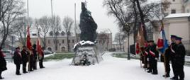 Pomnik Jana Pawła II pod którym stoi pięć pocztów sztandarowych, pada śnieg