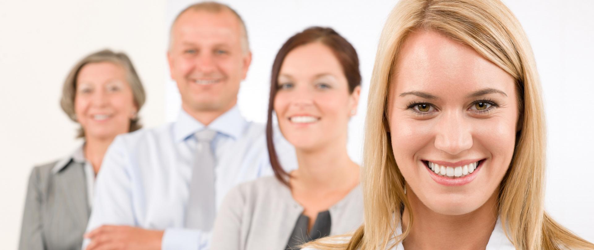 Młoda uśmiechnięta kobieta a w tle trzy inne uśmiechnięte osoby