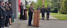 Strażacy w mundurach wyjściowych na placu apelowym. Przy mównicy nadbryg. Jacek Kleszczewski - Śląski Komendant Wojewódzki, a w tle spiker i poczet flagowy przy maszcie.