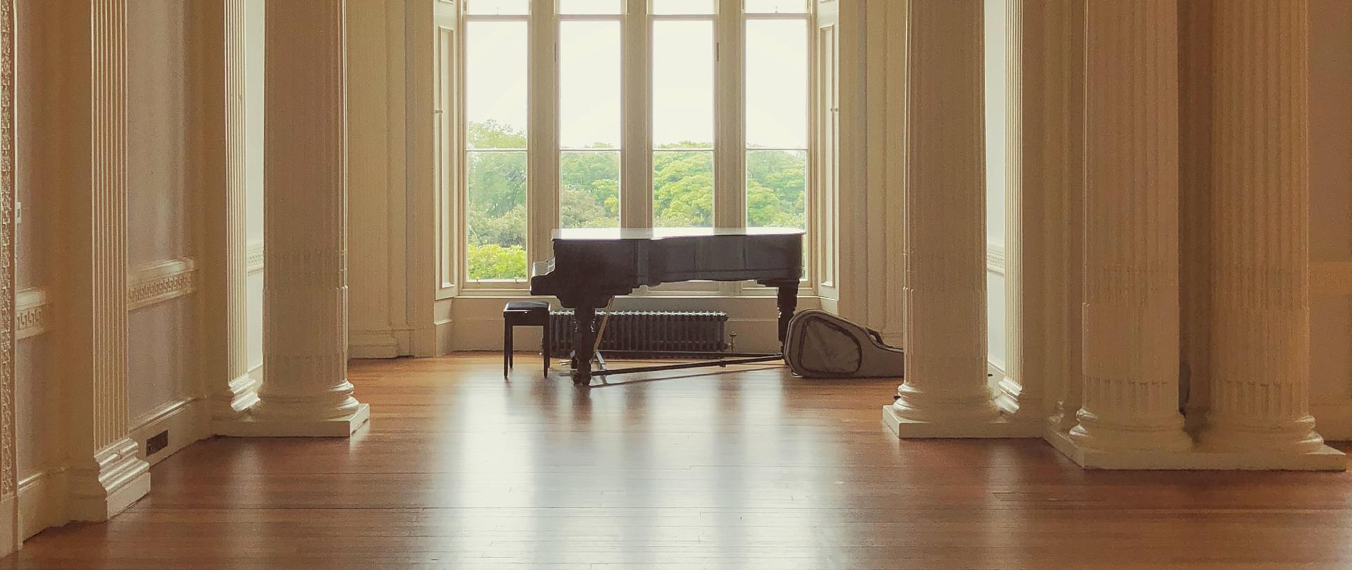 zdjęcie przedstawiające dużą salę z fortepianem ustawionym na tle okna w przestronnej, pustej sali