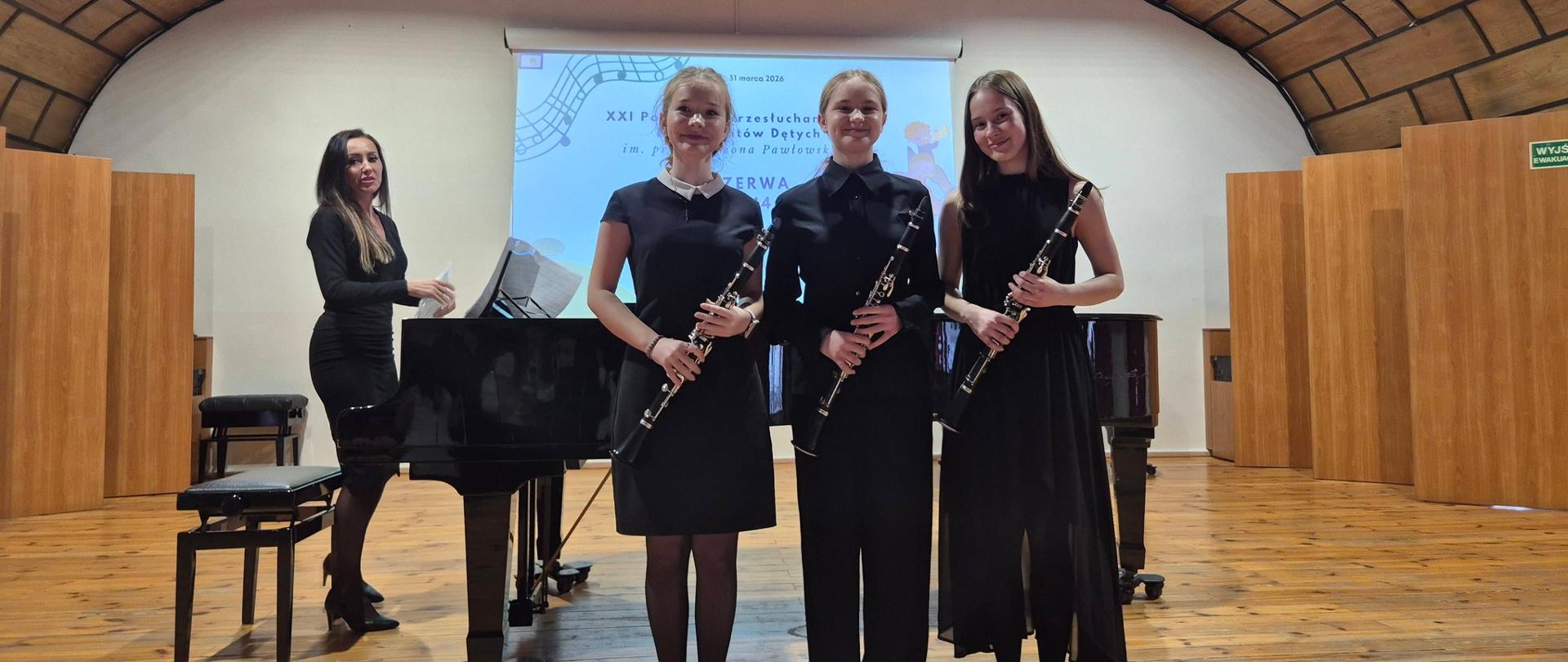 Uczennice trio klarnetowego pozują z instrumentami na sali koncertowej w Lęborku. W tle Urszula Zakrzewska przy fortepiania