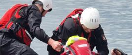Widać strażaków jak wyciągają z wody osobę poszkodowaną na łódź