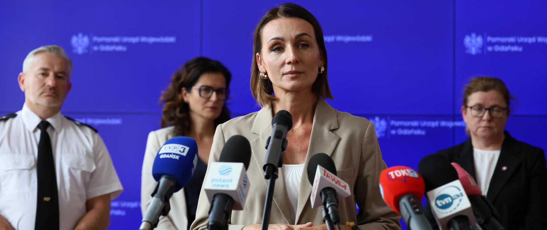 Kobieta (wojewoda) stoi przed mikrofonem, za nią stoją inne osoby