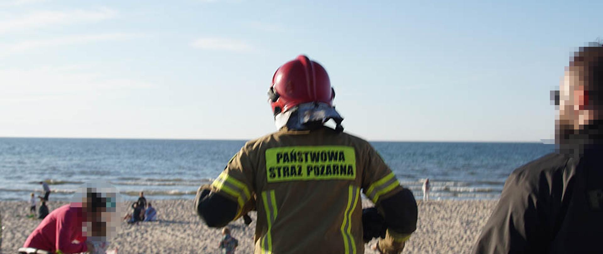 Strażak na plaży , w tle widać ludzi i wodę.