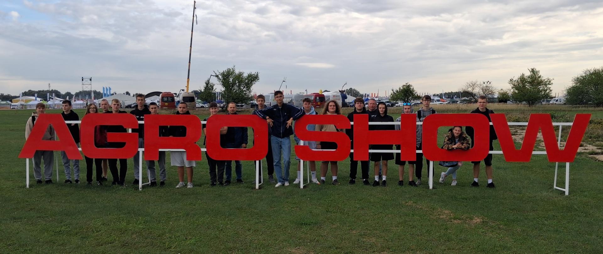 Grupa uczniów pozuje przy napisie „AGROSHOW” podczas wyjazdu edukacyjnego.