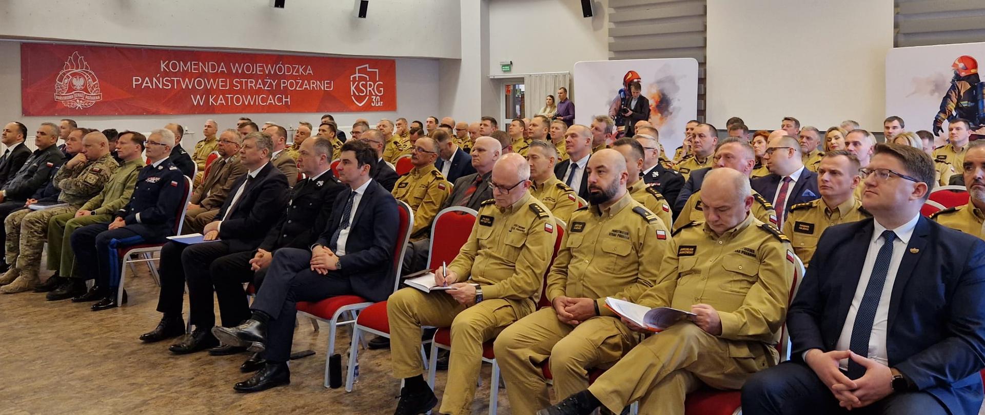 Grupa ludzi siedząca na krzesłach na dużej sali.