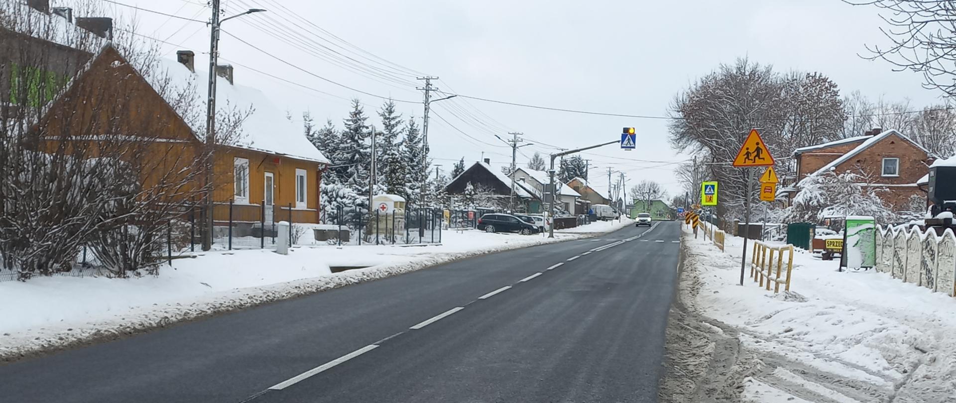 DK78 Moskorzew - droga jednojezdniowa, domy przy drodze, śnieg obok drogi, w oddali oznakowane przejście dla pieszych 