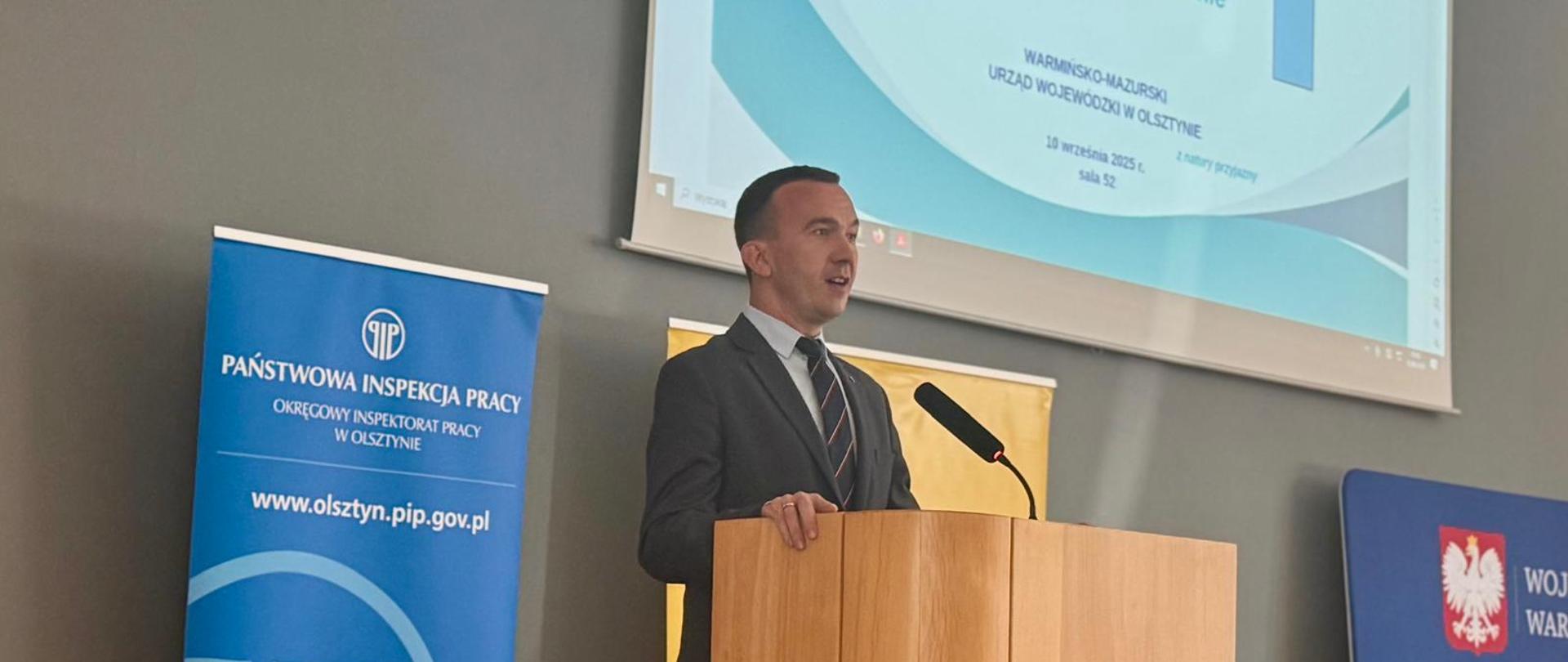 Mężczyzna stoi na scenie i przemawia z mównicy 