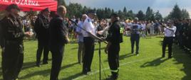 Zdjęcie przedstawia wręczenie pucharu druhowi OSP przez Zastępcę Komendanta Wojewódzkiego PSP. Dookoła stoją strażacy oraz osoby cywilne.