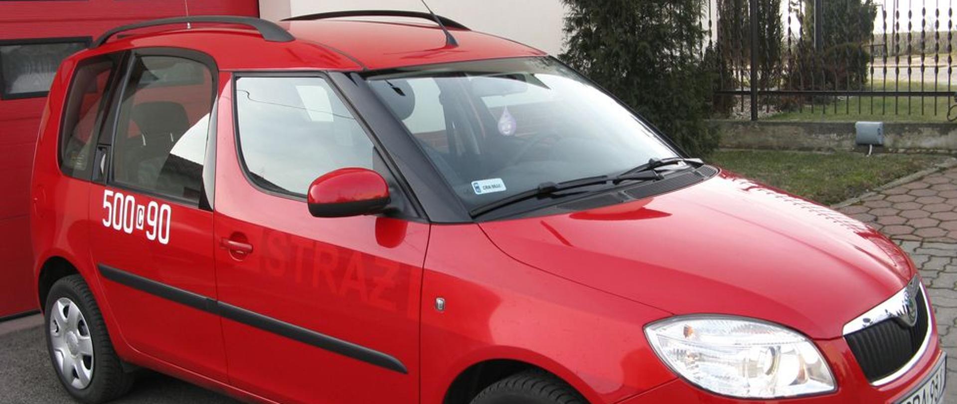 Zdjęcie przedstawia czerwony samochód SLKW Skoda Roomster na tle garażu KP PSP.