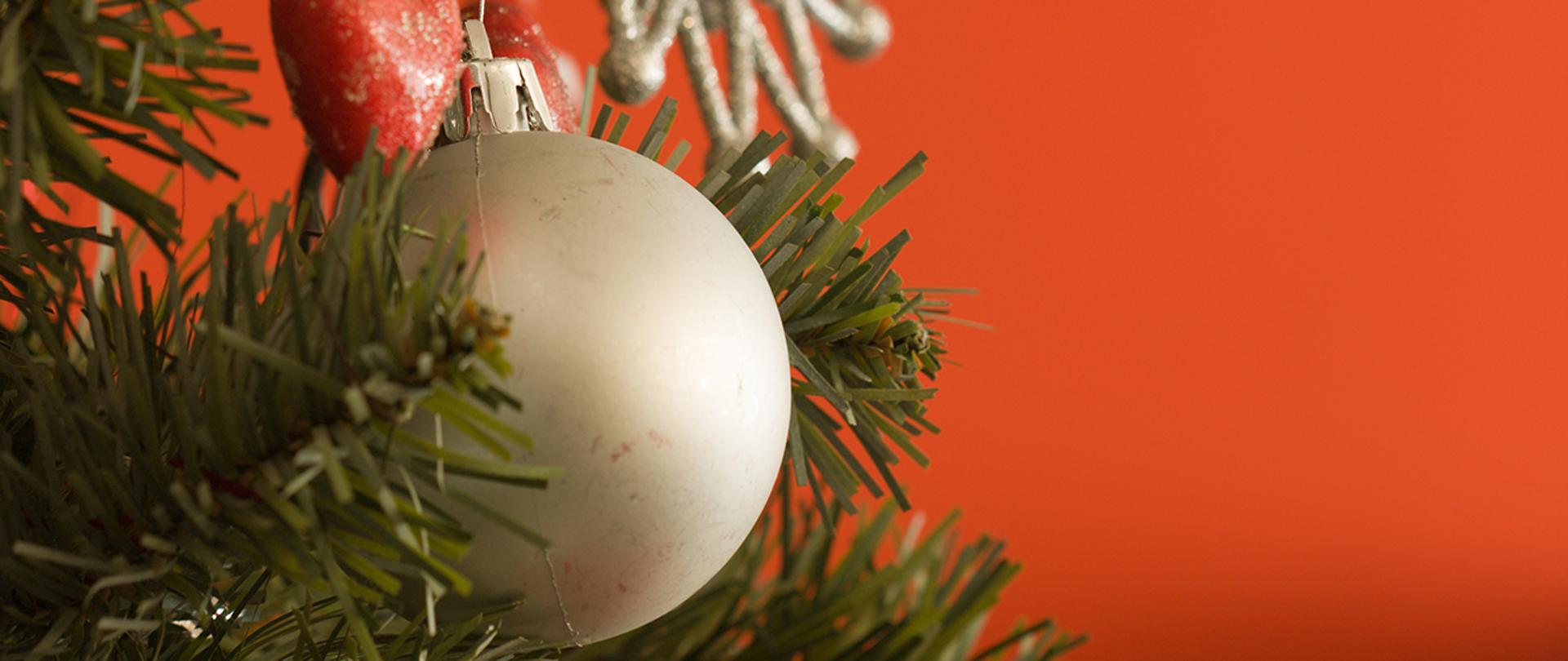 Karta bożonarodzeniowa, na czerwonym tle, z lewej strony gałązka choinki, na niej bańki choinkowe