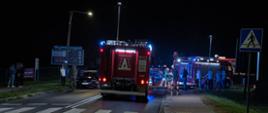 Zdjęcie przedstawia samochody służb ratowniczych stojące na drodze podczas działań ratowniczo-gaśniczych. Na poboczu zgromadzeni ludzie, świadkowie zdarzenia. 