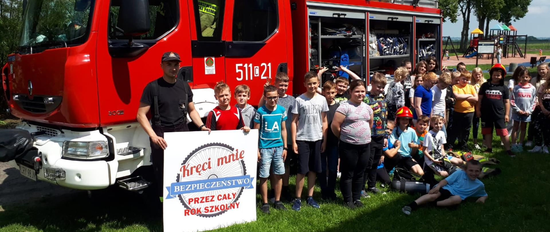Zdjęcie przedstawia dzieci ze Szkoły Podstawowej w Borzyminie stojące na tle ciężarowego samochodu pożarniczego.