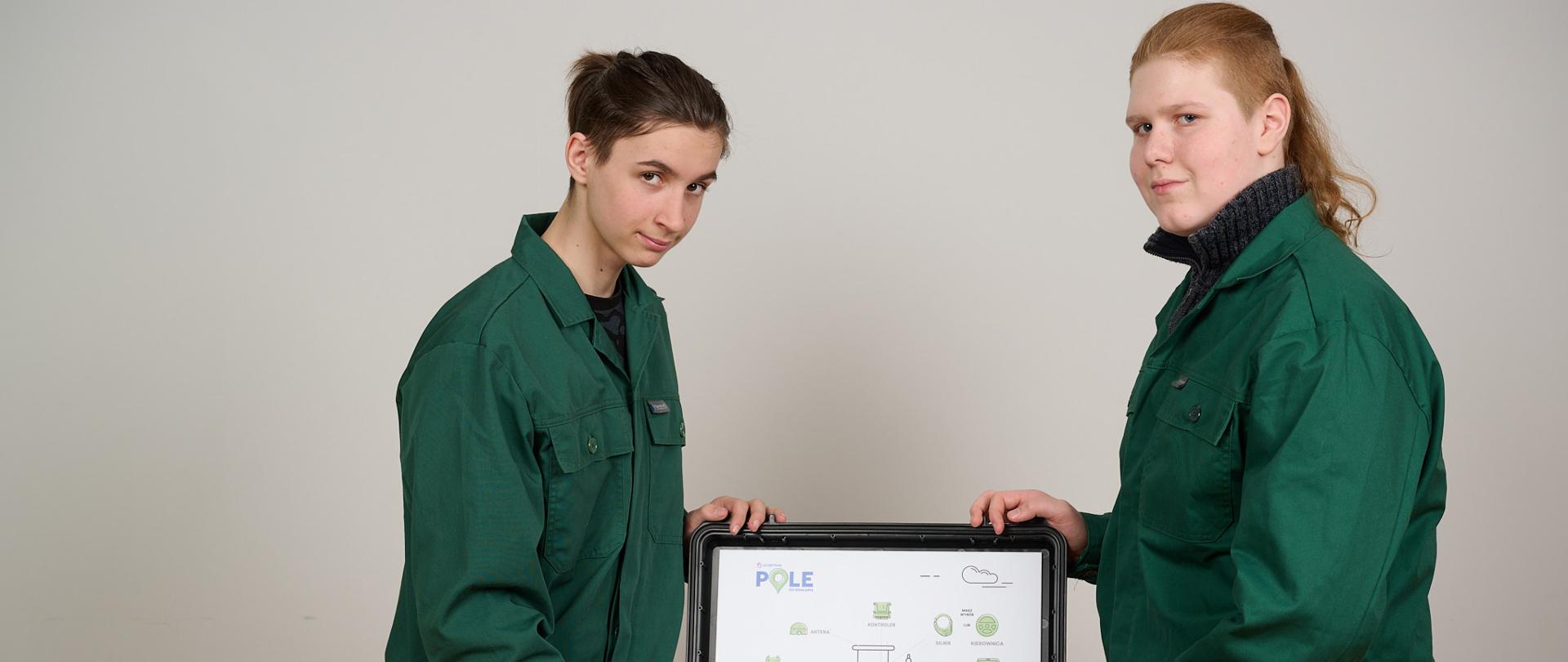 Dwóch chłopców trzyma rękoma walizkę położoną na stoliku. W Walizce jest sprzęt wyświetlający system polowy dla rolnictwa