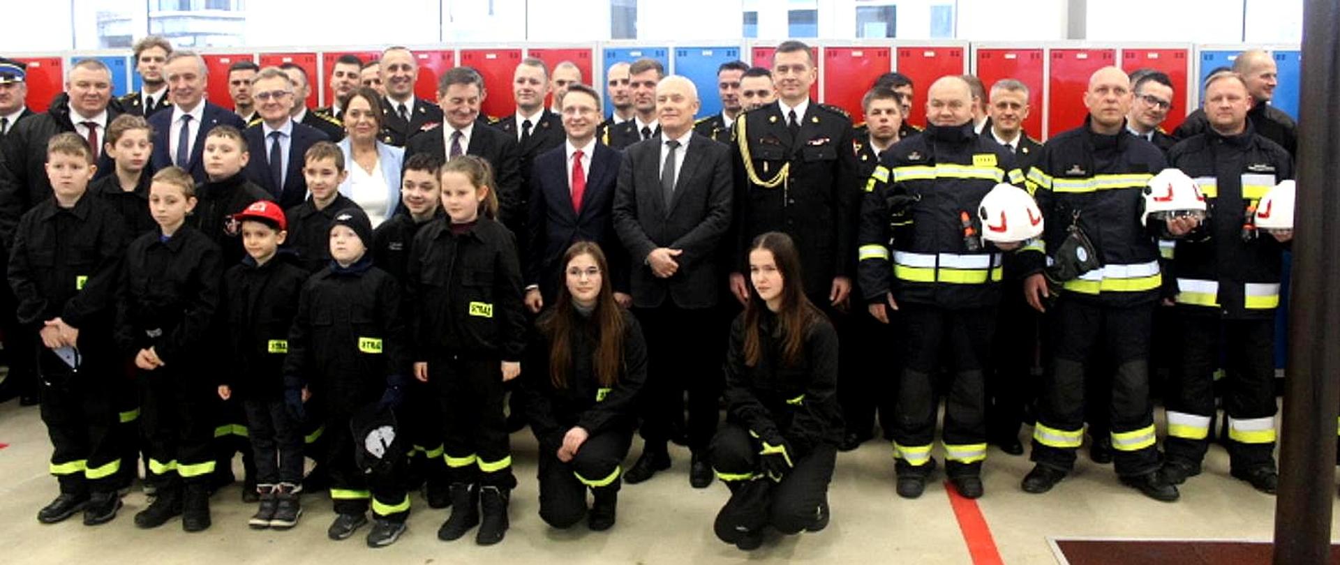 Zdjęcie zrobione w garażu jednostki PSP w Lesku. Na zdjęciu ustawieni do zbiorowego zdjęcia uczestnicy uroczystości.