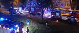 Pożar mieszkania przy ul. Rostockiej, wiać strażaków rozwijających węzę pożarnicze oraz cztery samochody pożarnicze stojące przy budynku.