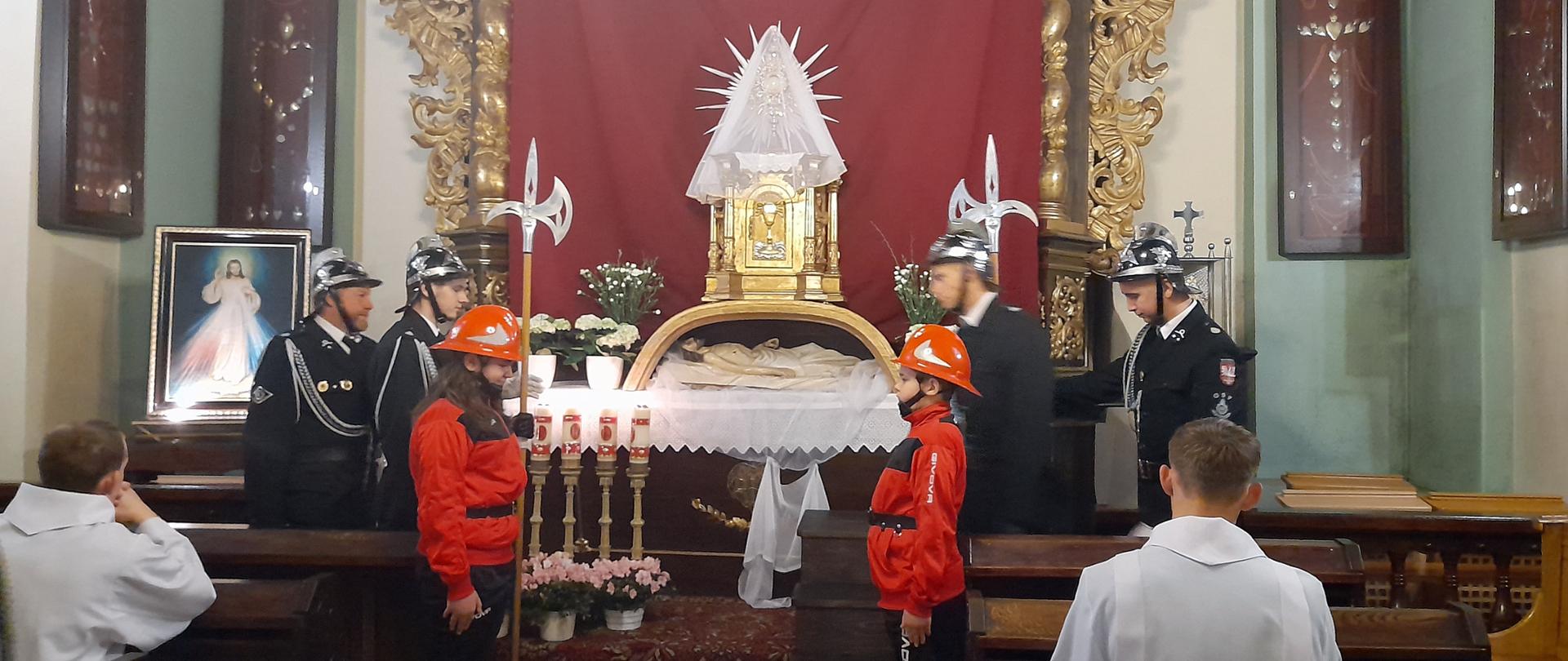 Widok z tyłu. Warta czterech strażaków OSP i dwóch członków MDP przy Grobie Pańskim. Na drugim planie Grób Chrystusa.