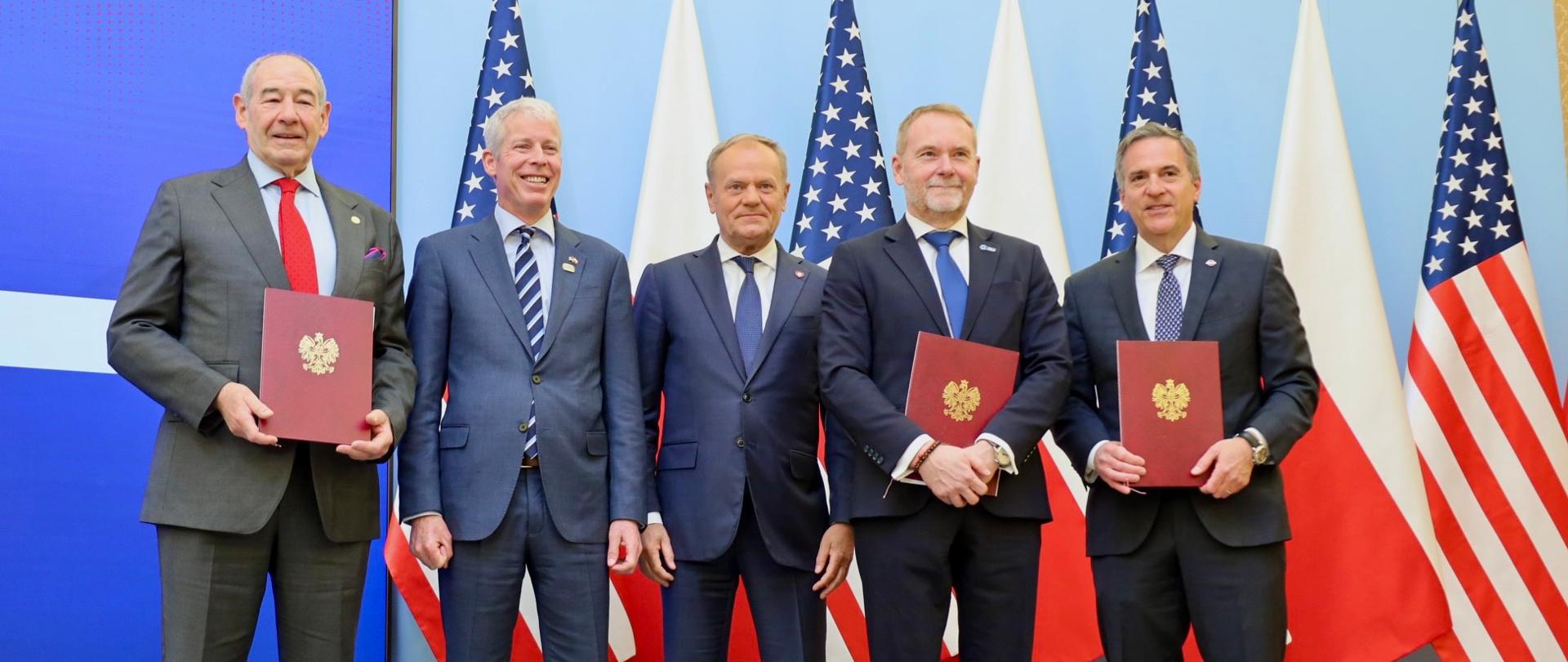 pięciu mężczyzn stoi na tle polskich i amerykańskich flag