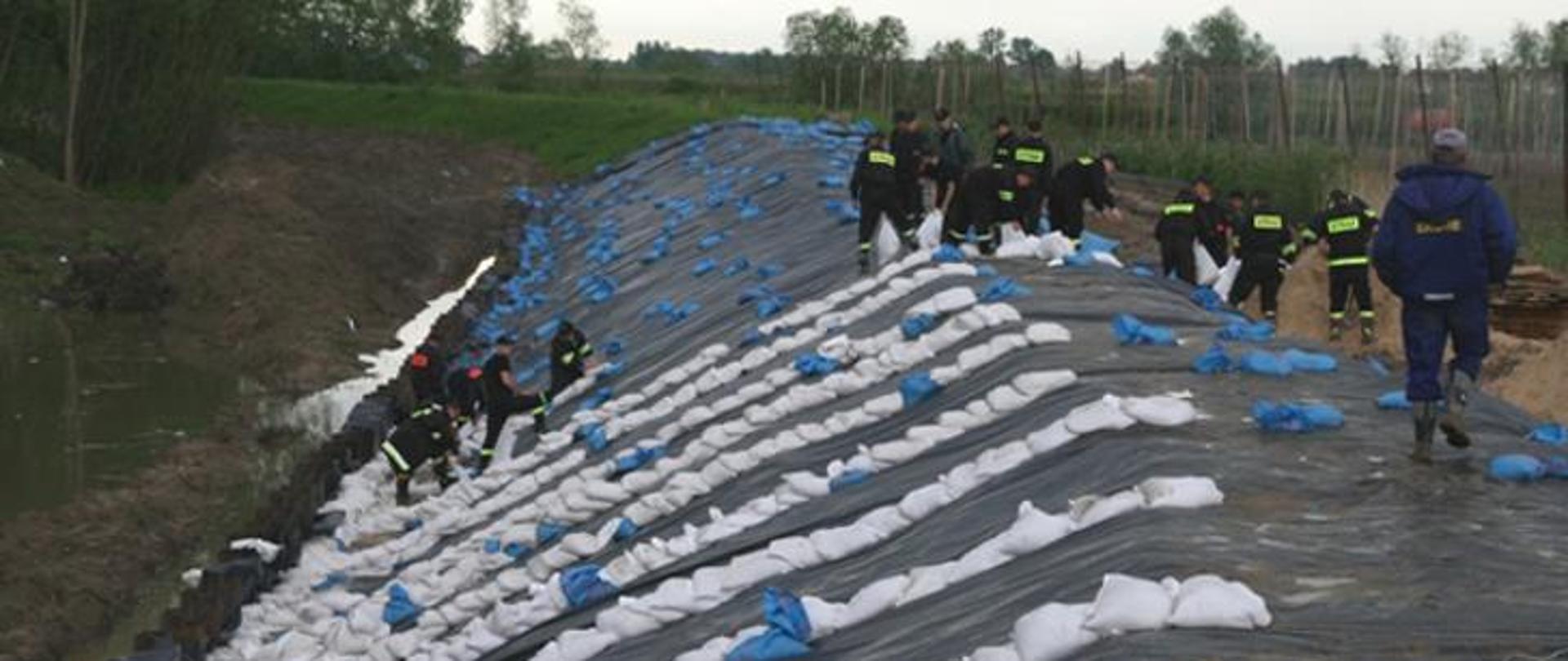 Strażacy układają worki umacniające wał