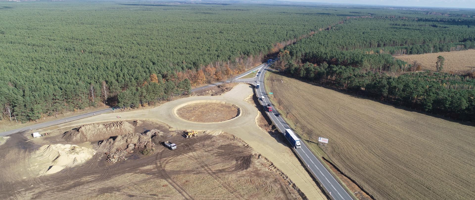 Zarys ronda na etapie prac ziemnych widoczny z lotu ptaka. Rondo wkomponowane u styku dwóch dróg. Dookoła lasy i pola.