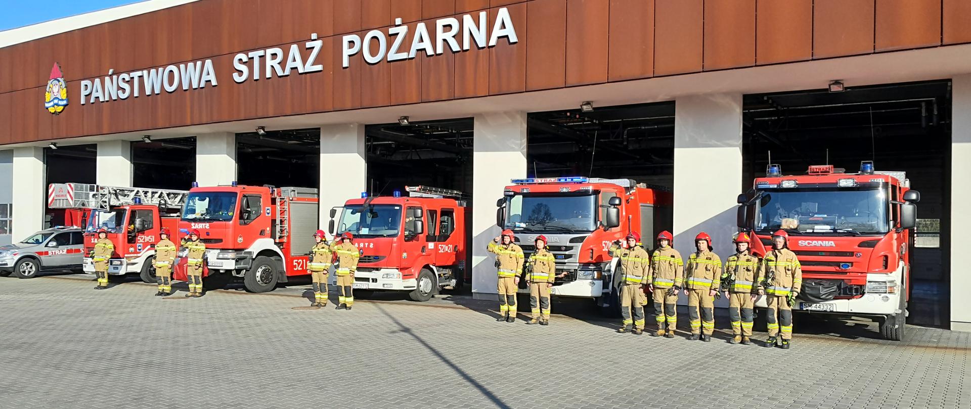 Mysłowiccy strażacy oddają cześć bohaterskim strażakom z Ukrainy na tle komendy miejskiej i samochodów ratowniczo - gaśniczych.