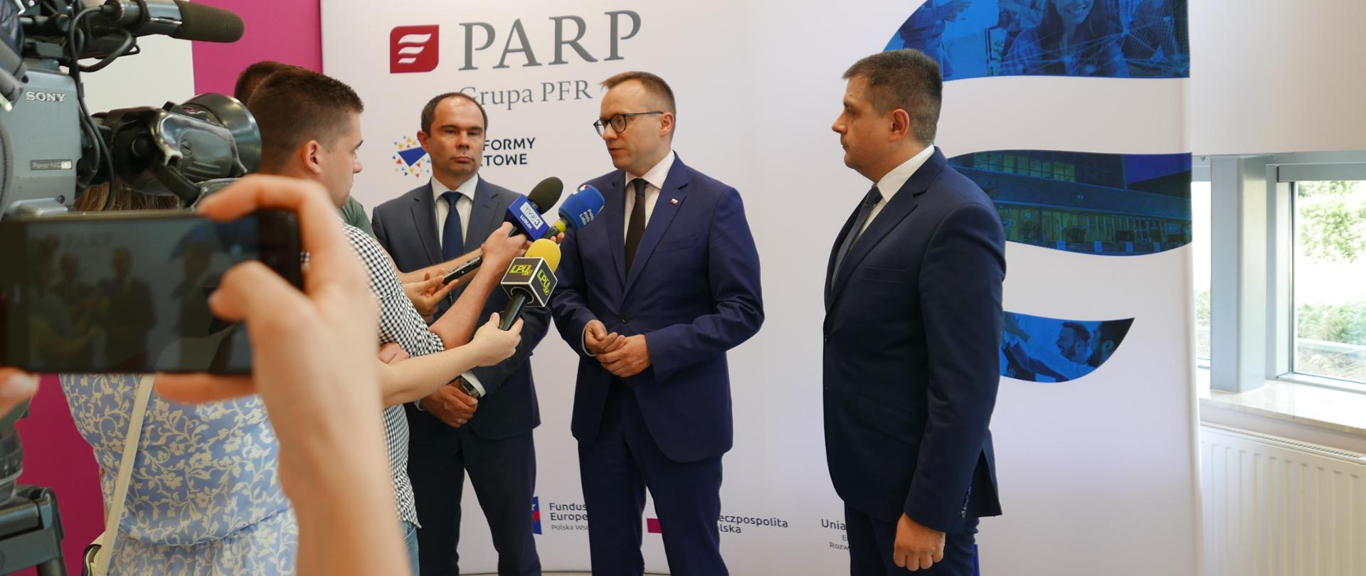 wiceminister Artur Soboń mówi do mikrofonów trzymanych przez dziennikarzy