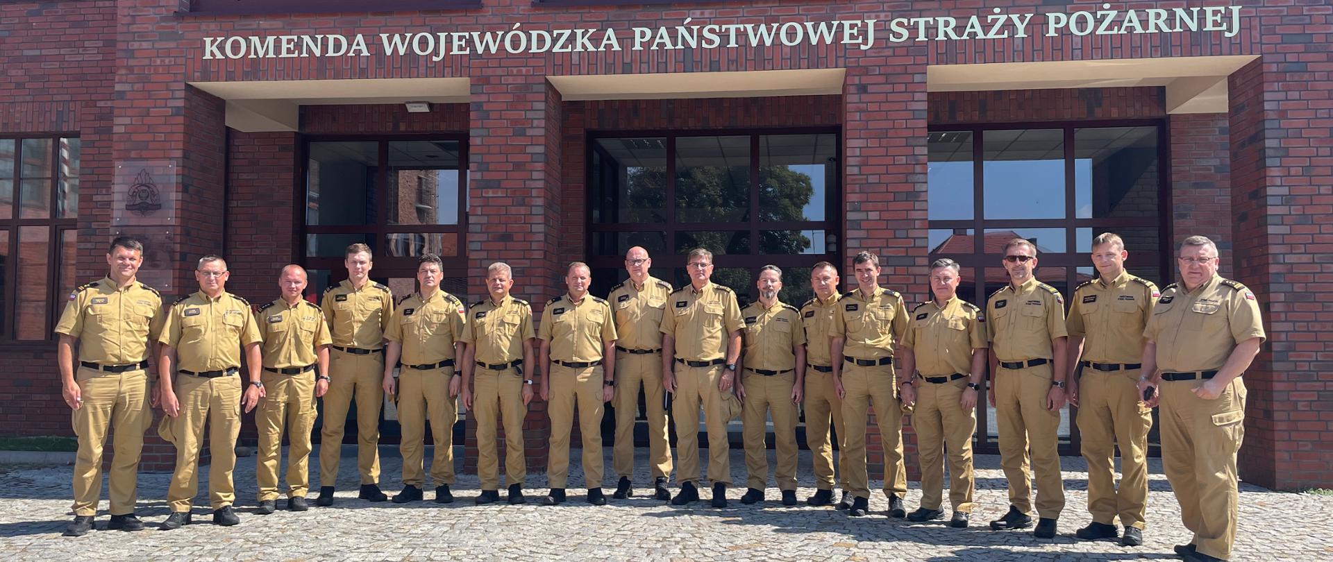 Funkcjonariusze Państwowej Straży Pożarnej stojąc przed budynkiem.