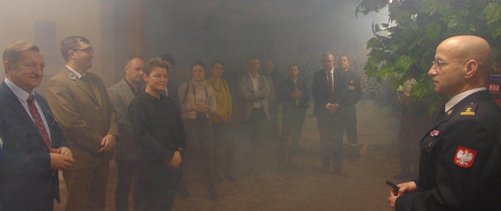 w zadymionej sali edukacyjnej komendant powiatowy przemawia do grupy ludzi