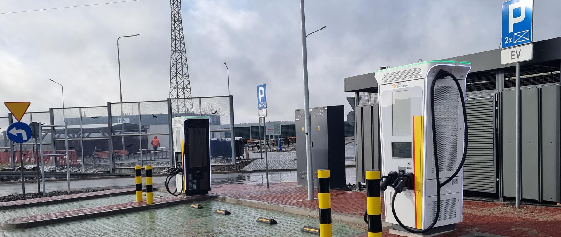 Stacje ładowania pojazdów elektrycznych - dwa białe dystrybutory przy miejscach do parkowania 