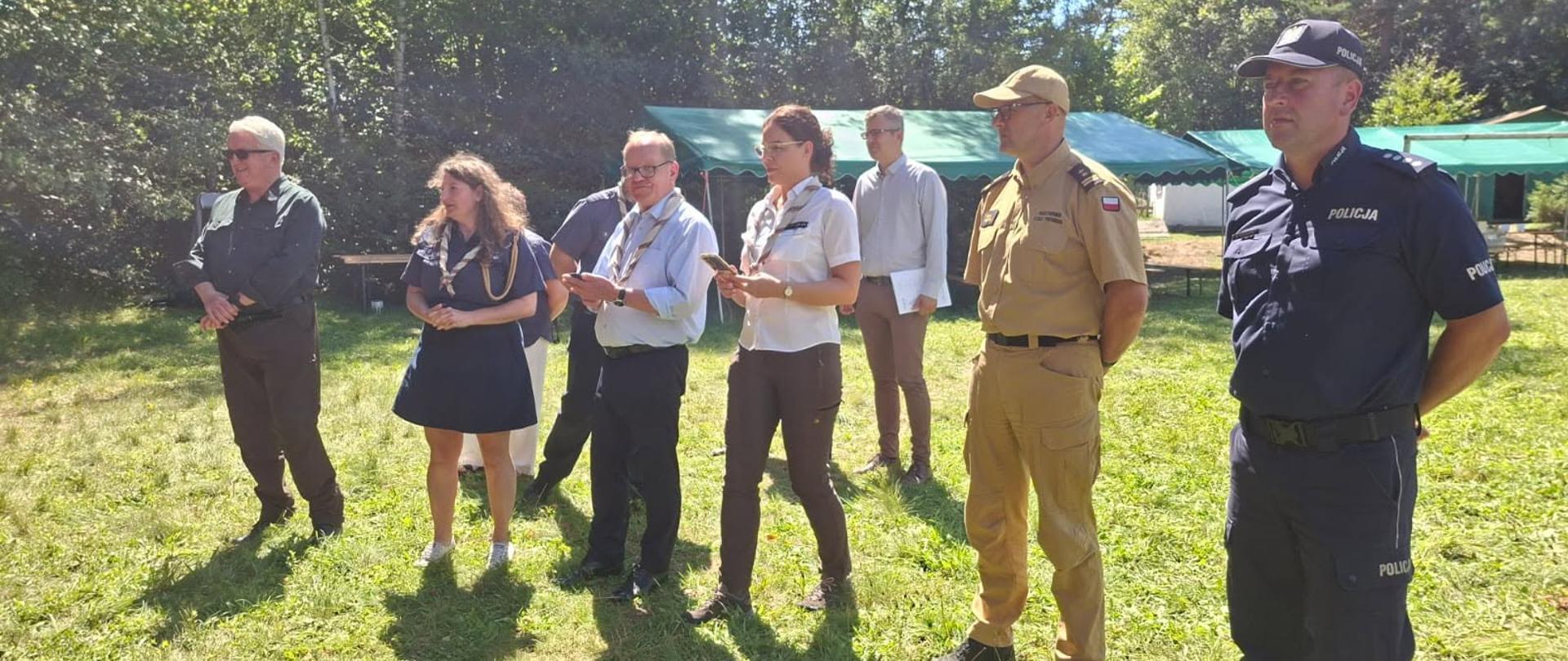 Zdjęcie przedstawia przedstawicieli Chorągwi Podkarpackiej ZHP komendanta powiatowego PSP oraz policjanta na terenie obozowiska. 