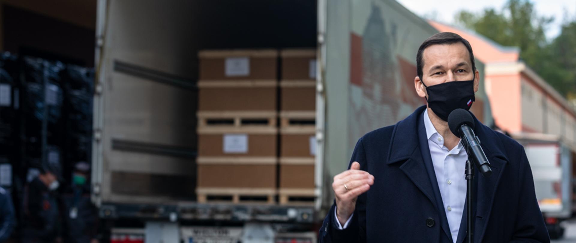 Premier Mateusz Morawiecki na tle ciężarówki.