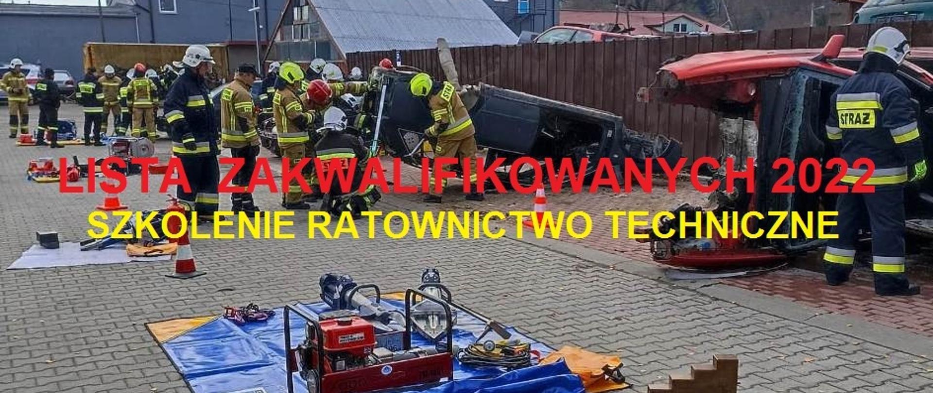 Kolorowa fotografia wykonana na zewnątrz w pochmurny dzień, naktórej widać kilka grup umundurowanych na bojowo strażaków. Ćwiczą ze sprzętem ratowniczym przy kilku wrakach pojazdów. Sprzęt przygotowany i zgromadzonych na niebieskich matach przed wrakami. W tle widoczne częściowo zabudowania, ogrodzenie i szare drzewa. Na środku fotografii czerwony napis na białym tle o treści: nowe szkolenie.